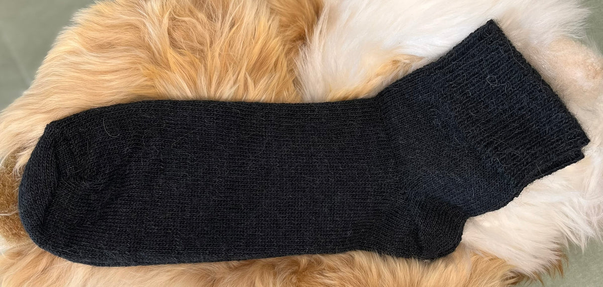Black alpaca ankle sock on a fluffy beige surface