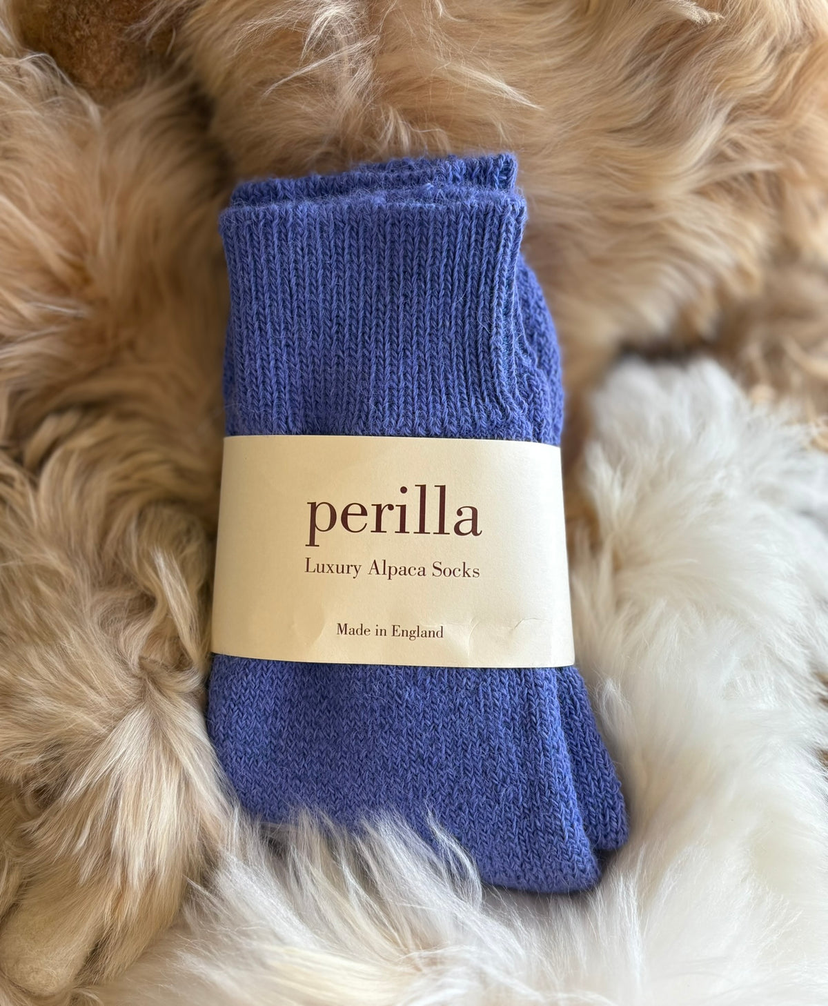 Mid Blue walking alpaca socks with 'perilla' label on a fluffy beige surface