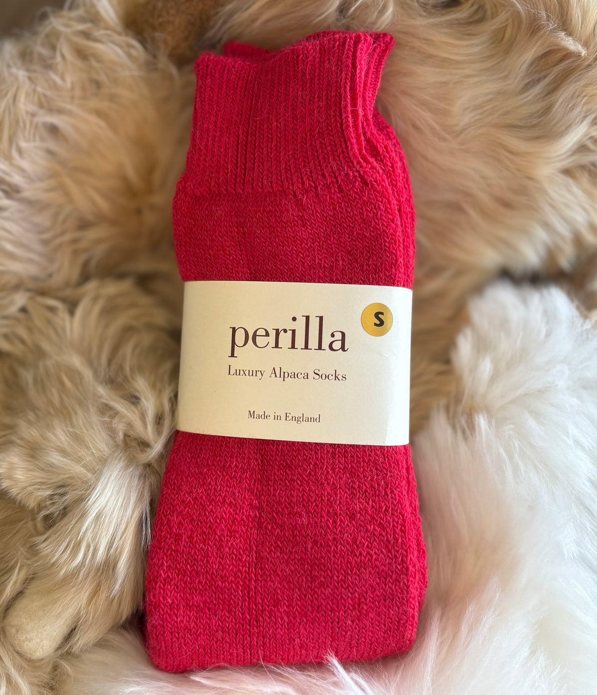 Raspberry walking alpaca sock with 'perilla' label on a fluffy beige surface