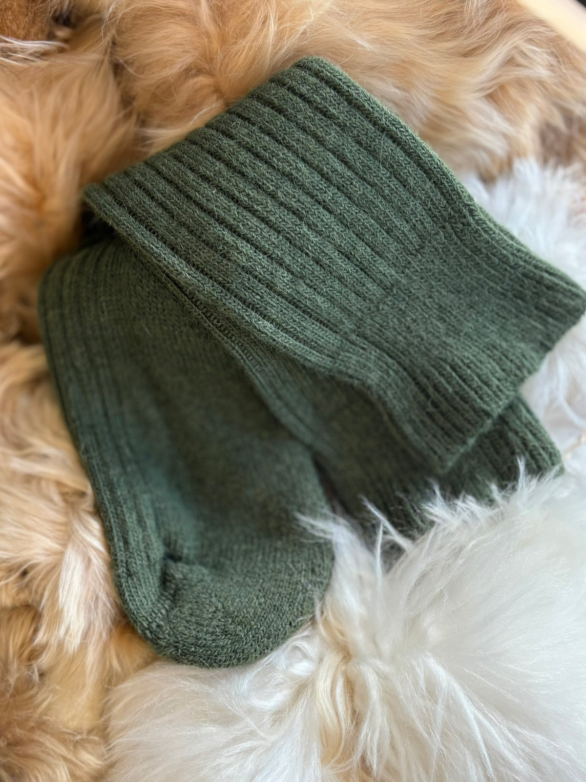 Pair of sedge green alpaca short ribbed socks on a fluffy white and beige surface