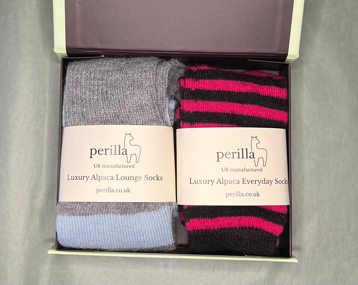 Gift box containing two pairs of Perilla Alpaca lounge socks. The left pair is a grey and pale blue striped, and the right pair has charcoal and raspberry stripes.