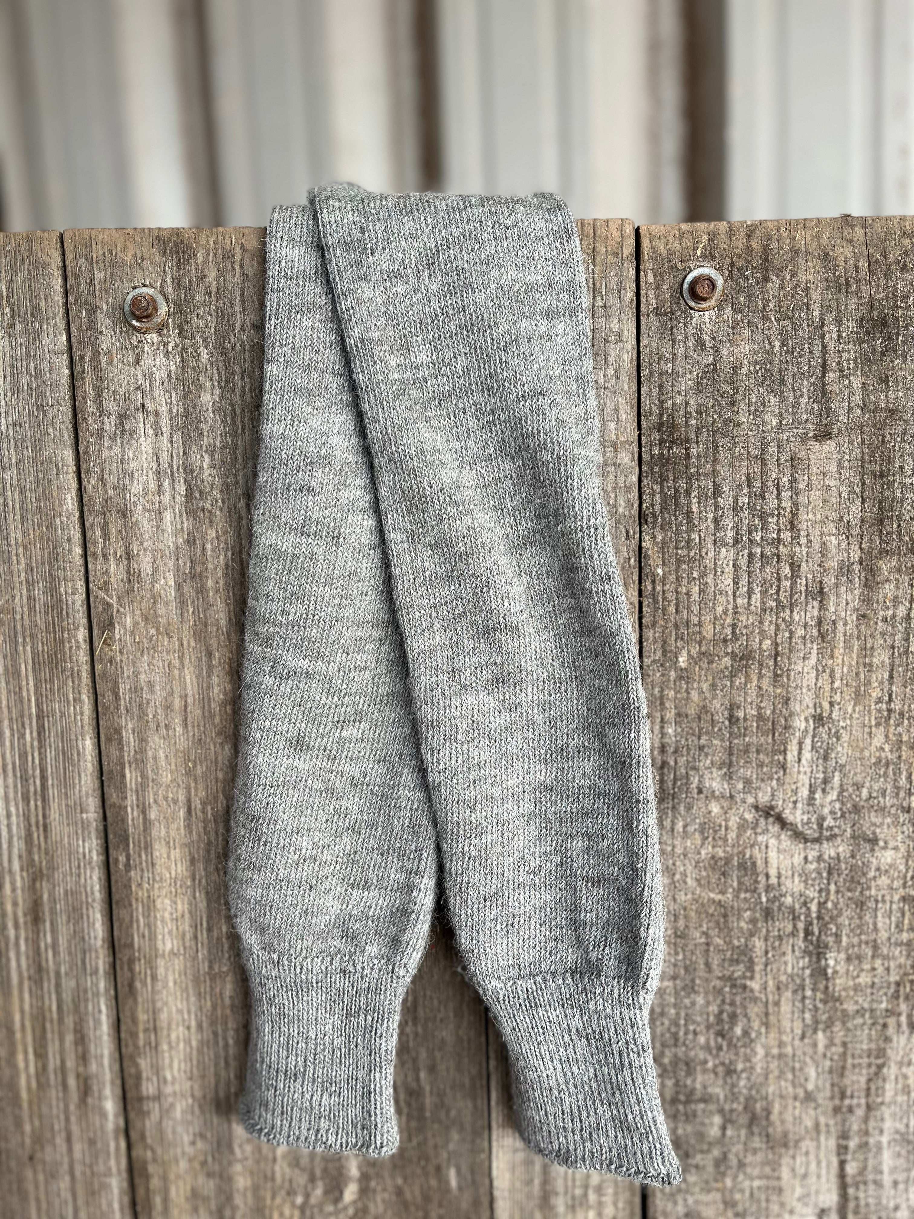 Grey long activity alpaca socks hanging on a wooden fence with a corrugated metal background