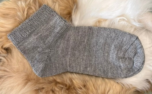 Grey alpaca trainer sock on a fluffy beige surface
