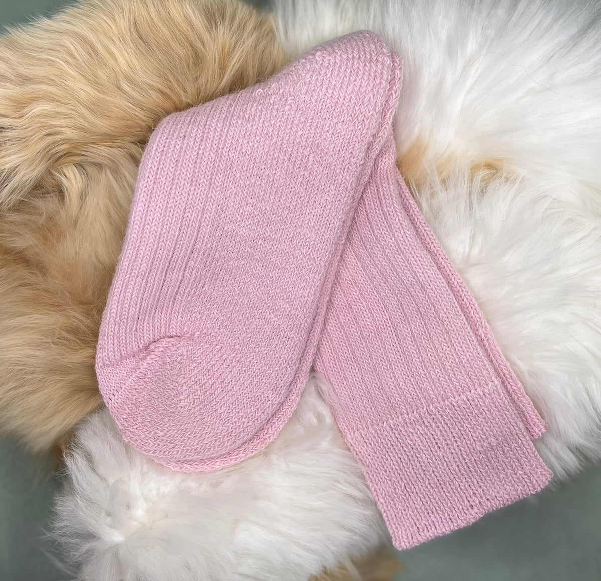 Pale Pink short ribbed alpaca socks on a fluffy white and beige surface