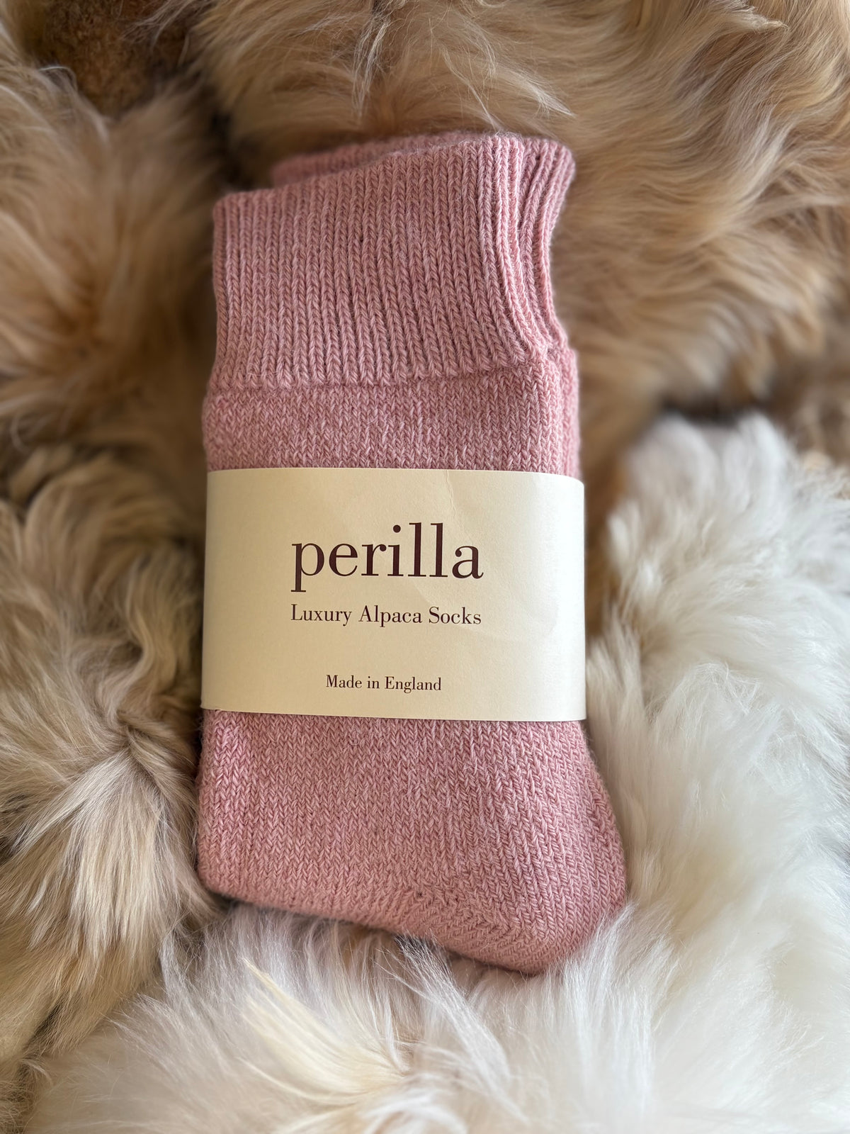 Pale Pink alpaca sock with 'perilla' label on a fluffy white surface