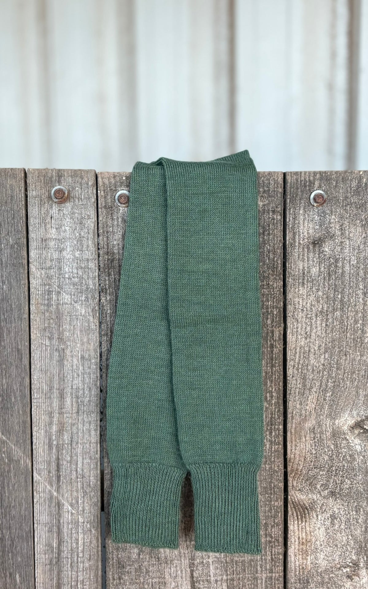 Sedge green knee length everyday socks on a wooden fence with a corrugated metal background