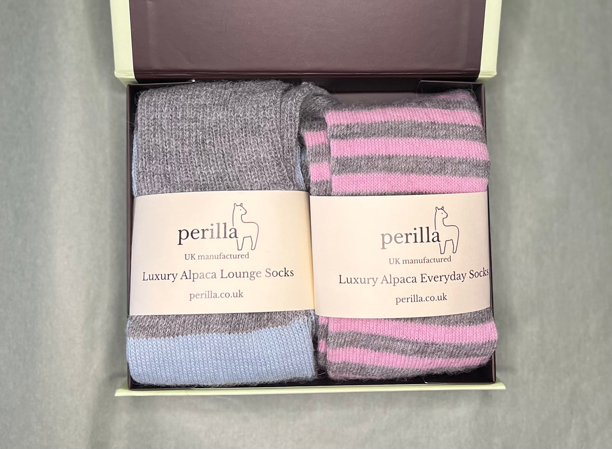 Gift box containing two pairs of Perilla Alpaca lounge socks. The left pair is grey and  a pale blue stripe, and the right pair is pink and grey striped.